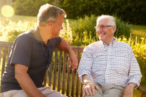 Two older adults enjoying a conversation in a bright, home-like common room with comfortable chairs.