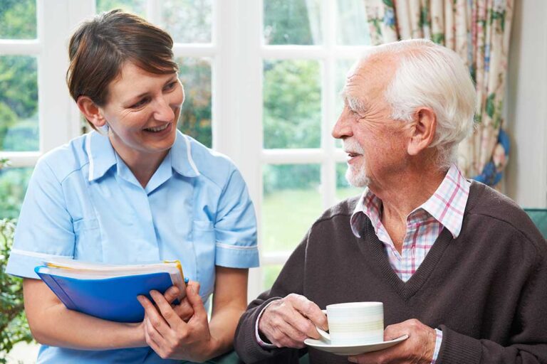 Older adult and caregiver discussing a daily care plan at a table in a bright assisted living apartment.